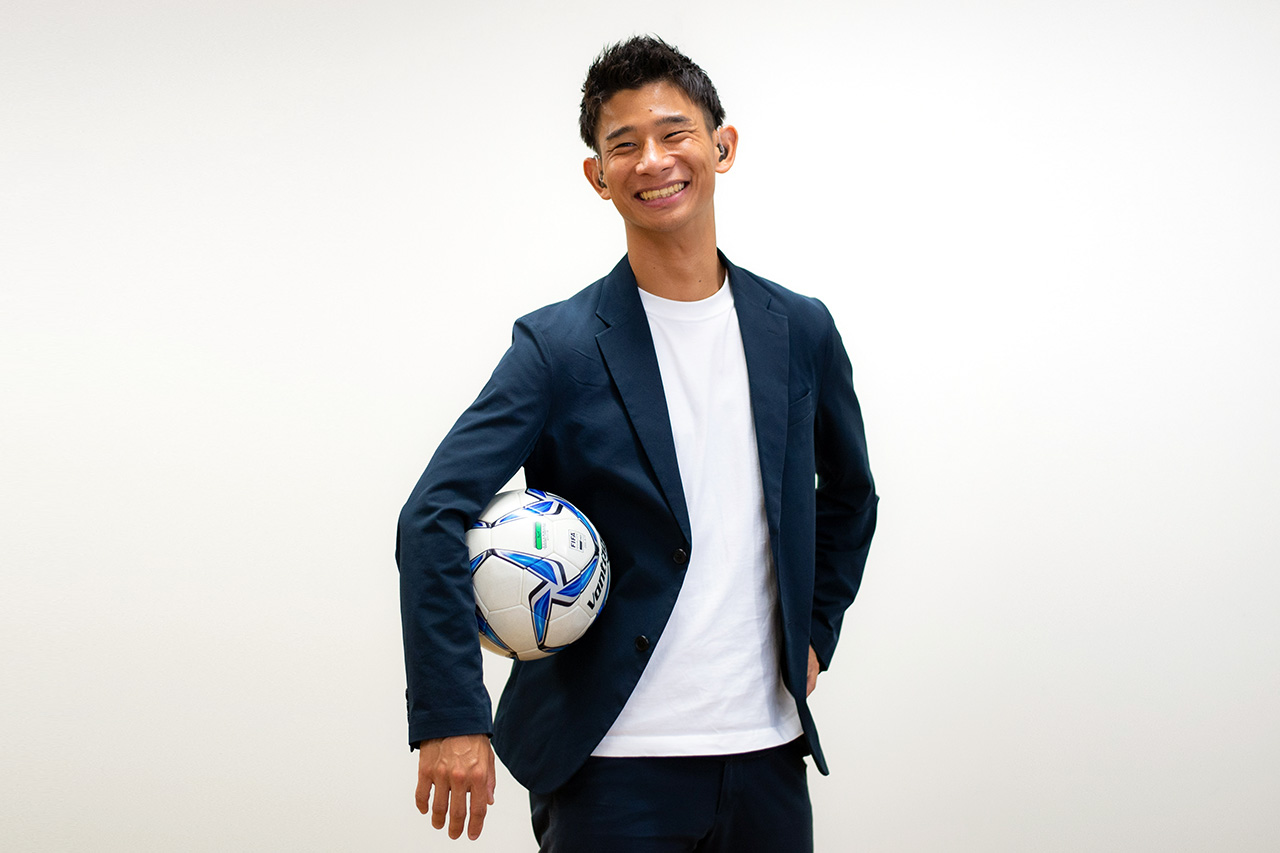 仲井健人選手がサッカーボールを脇に抱えて微笑んでいる